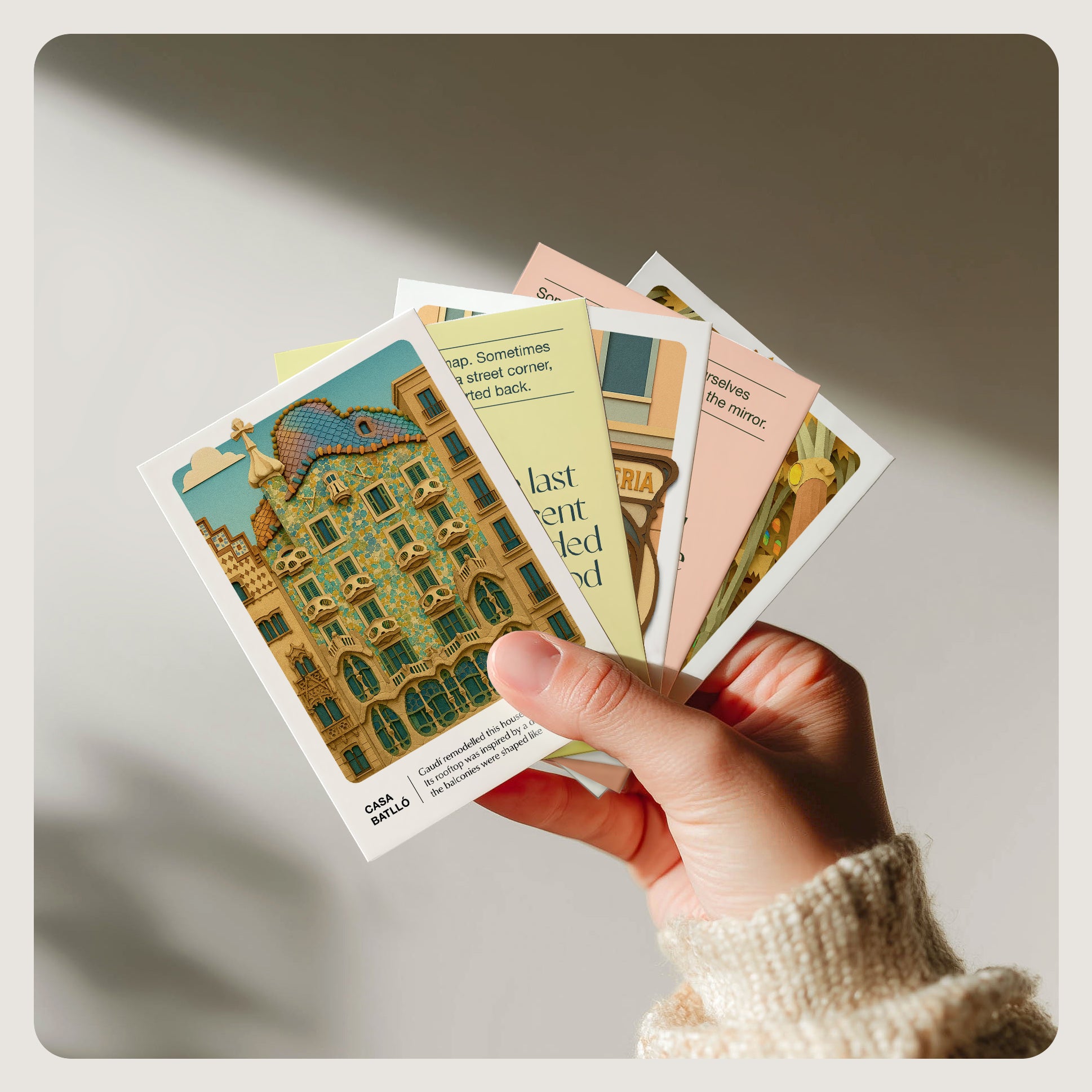 Hand holding several illustrated cards from the Barcelona Story Deck, with architectural artwork and soft-toned designs