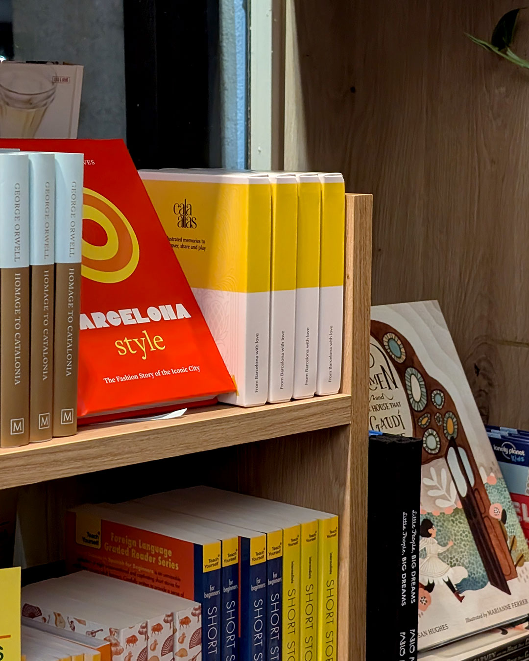 Row of Cala Atlas Barcelona Story Deck boxes displayed on a wooden shelf beside books