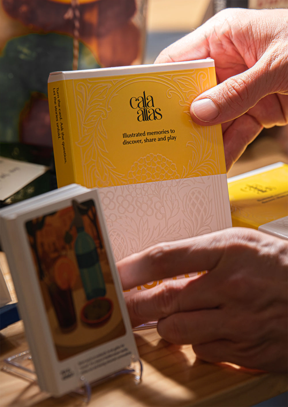 Hand holding a Cala Atlas yellow and white packaging from a display table, with other illustrated cards in the foreground