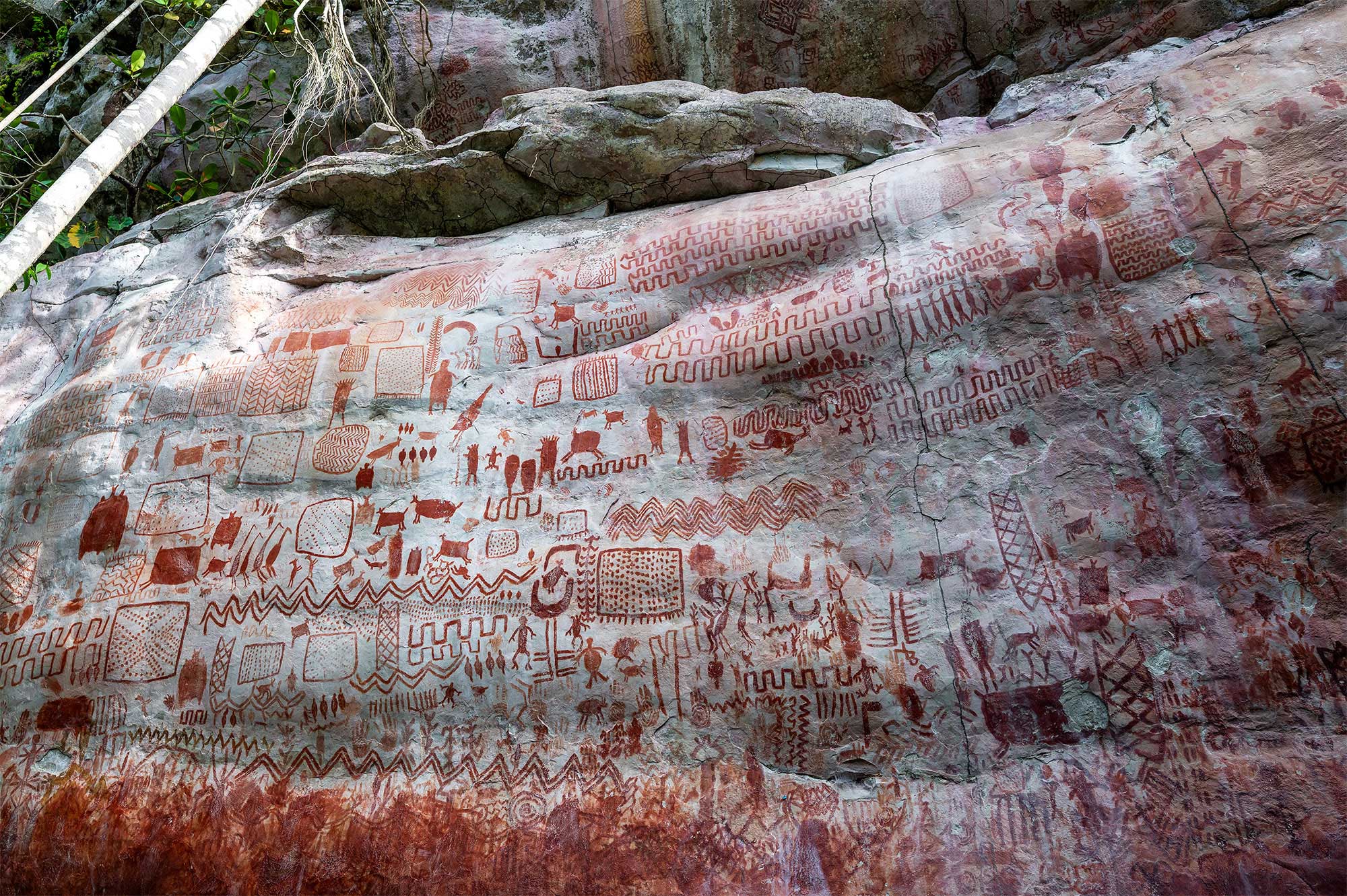 Extensive wall of red pictograms and geometric rock paintings on a large stone surface in cerro azul, Colombia