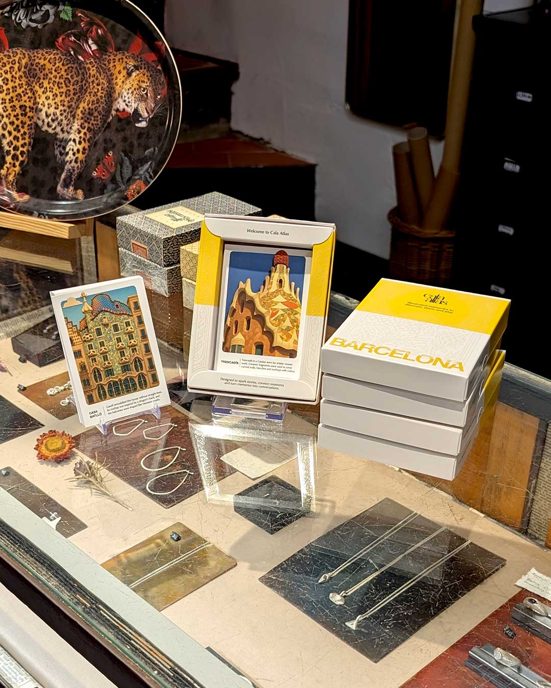 Cala Atlas Barcelona Story Deck box and two architectural illustrated cards arranged in a glass display with jewellery pieces