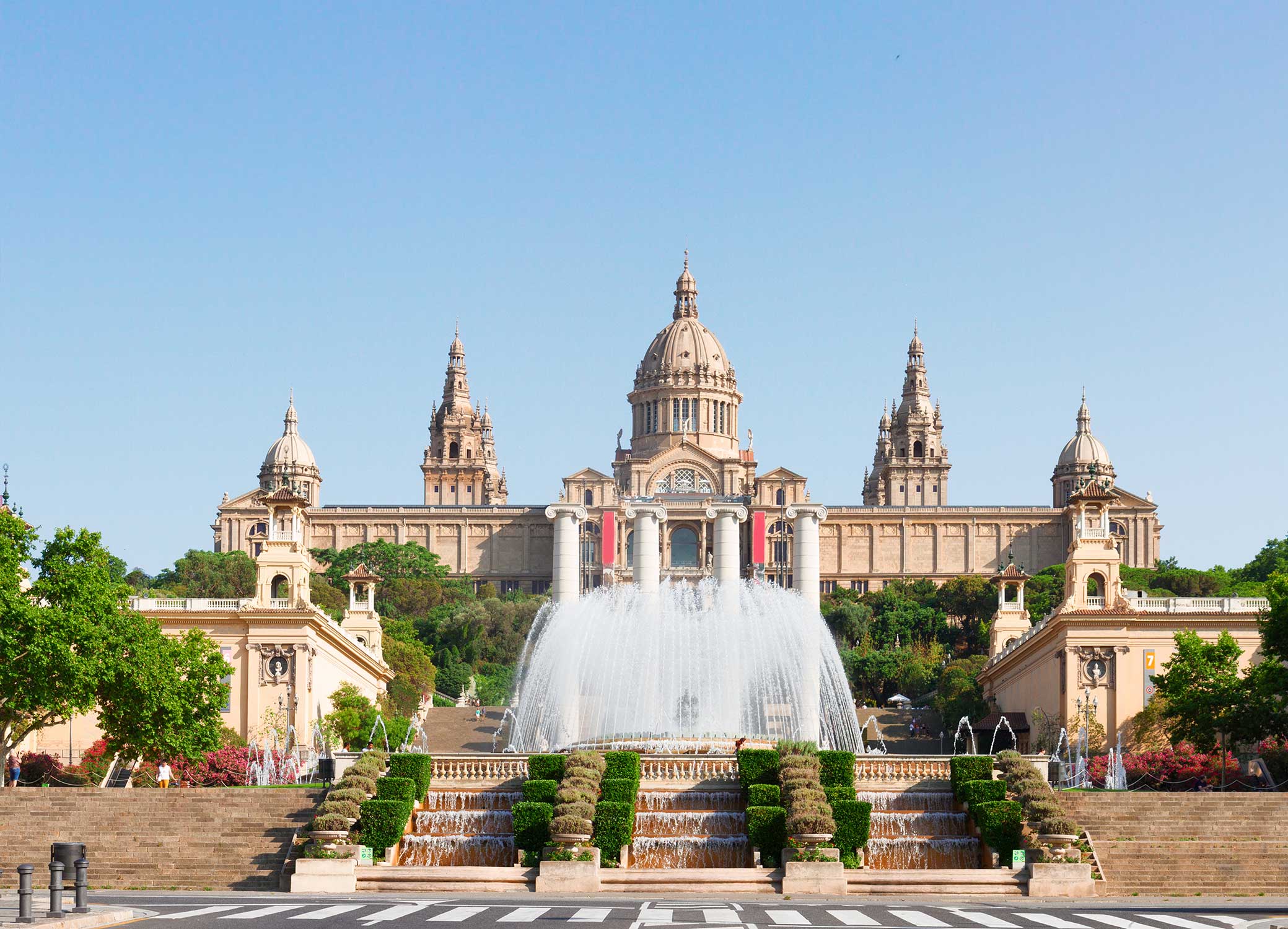 Front view of the Museu Nacional d’Art de Catalunya with cascading fountains and trimmed hedges on a clear day