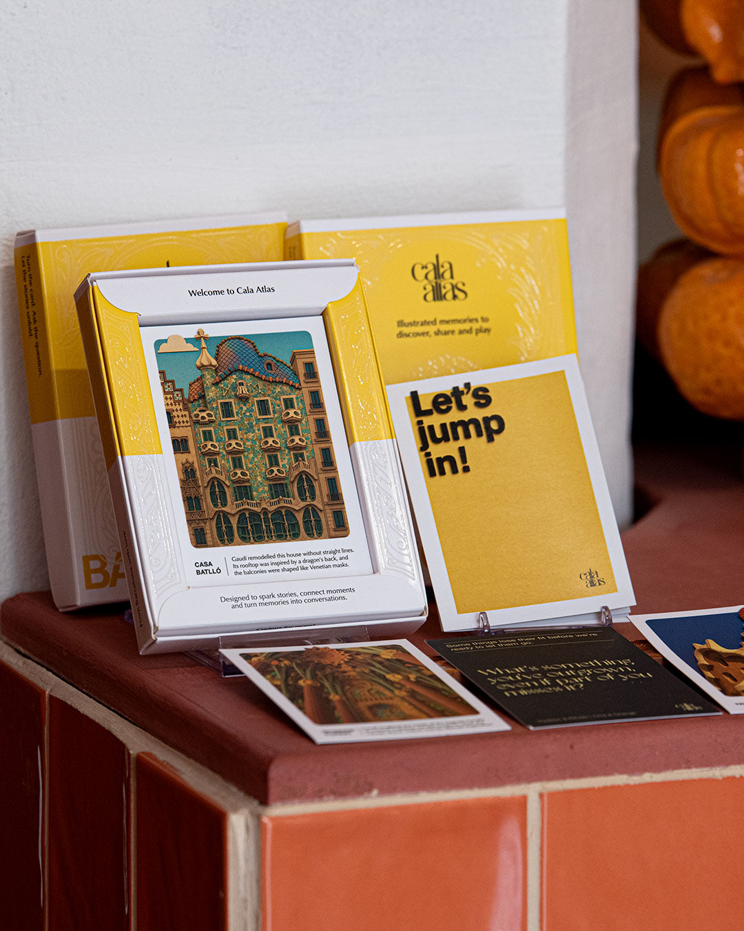 Cala Atlas Barcelona Story Deck, Casa Batlló illustrated card and yellow booklet displayed on terracotta tiles against a white wall