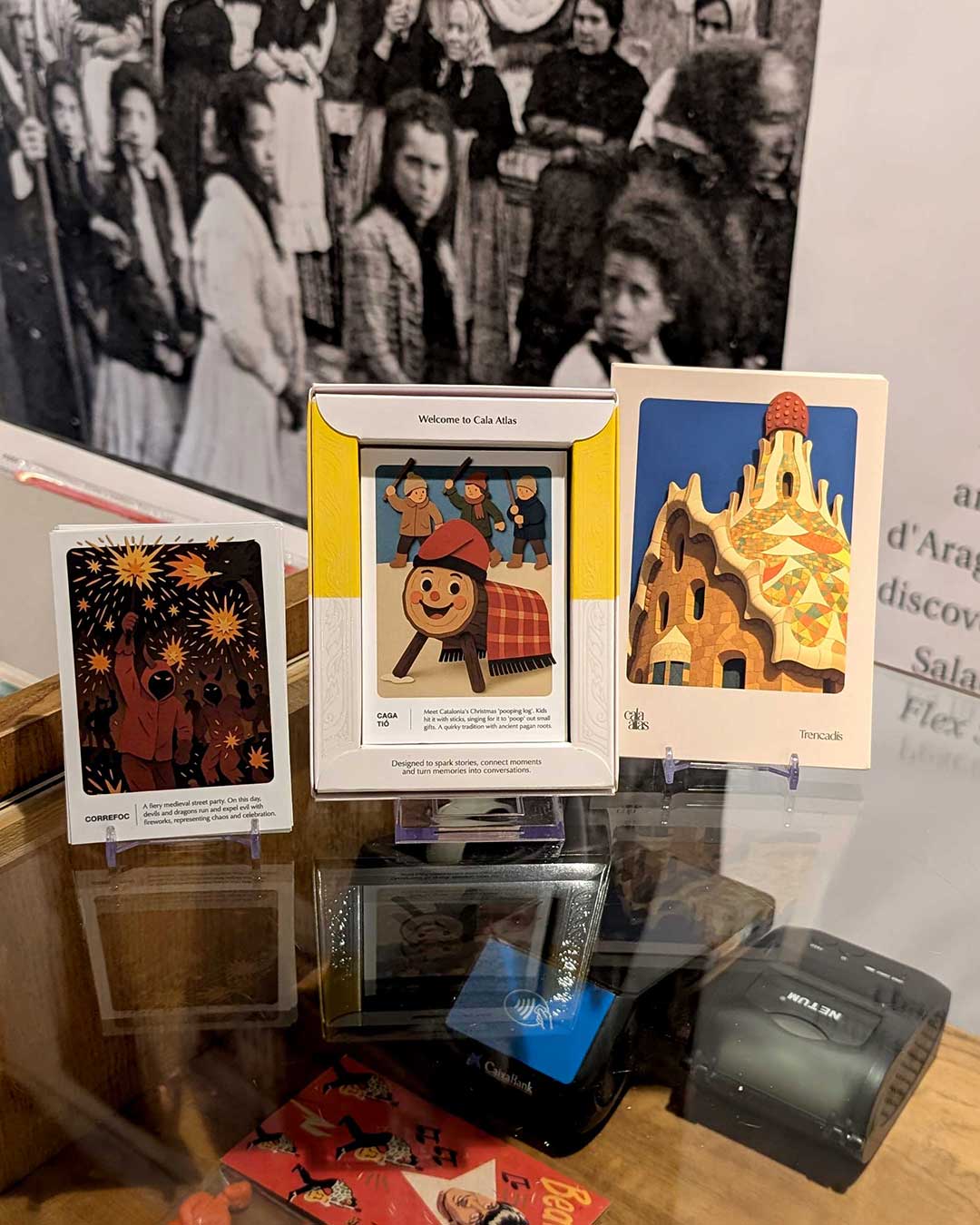Display of Cala Atlas Barcelona Story Deck box and two illustrated cards on a glass counter with vintage photo background
