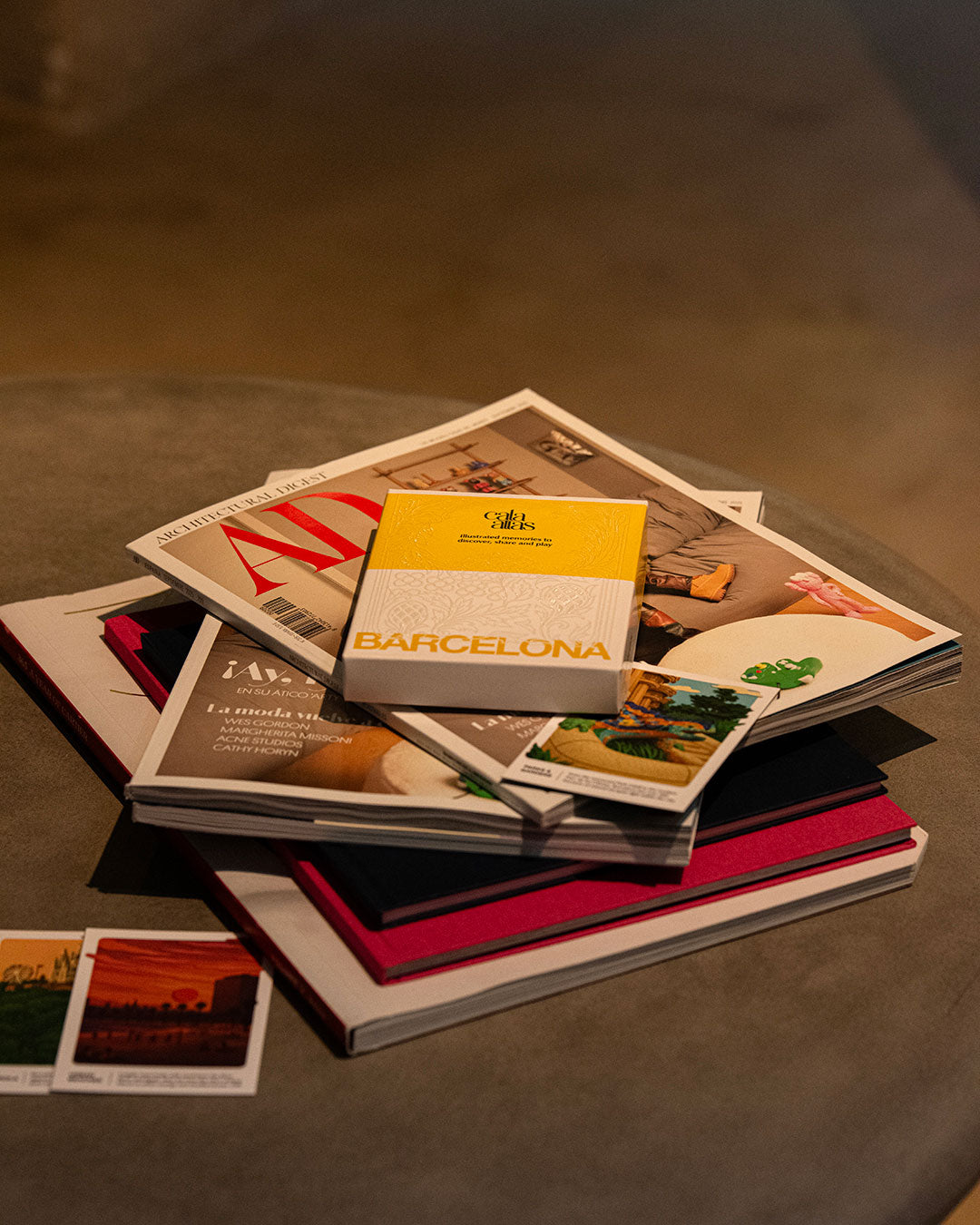Cala Atlas Barcelona yellow box resting on a stack of magazines with additional illustrated card on top.