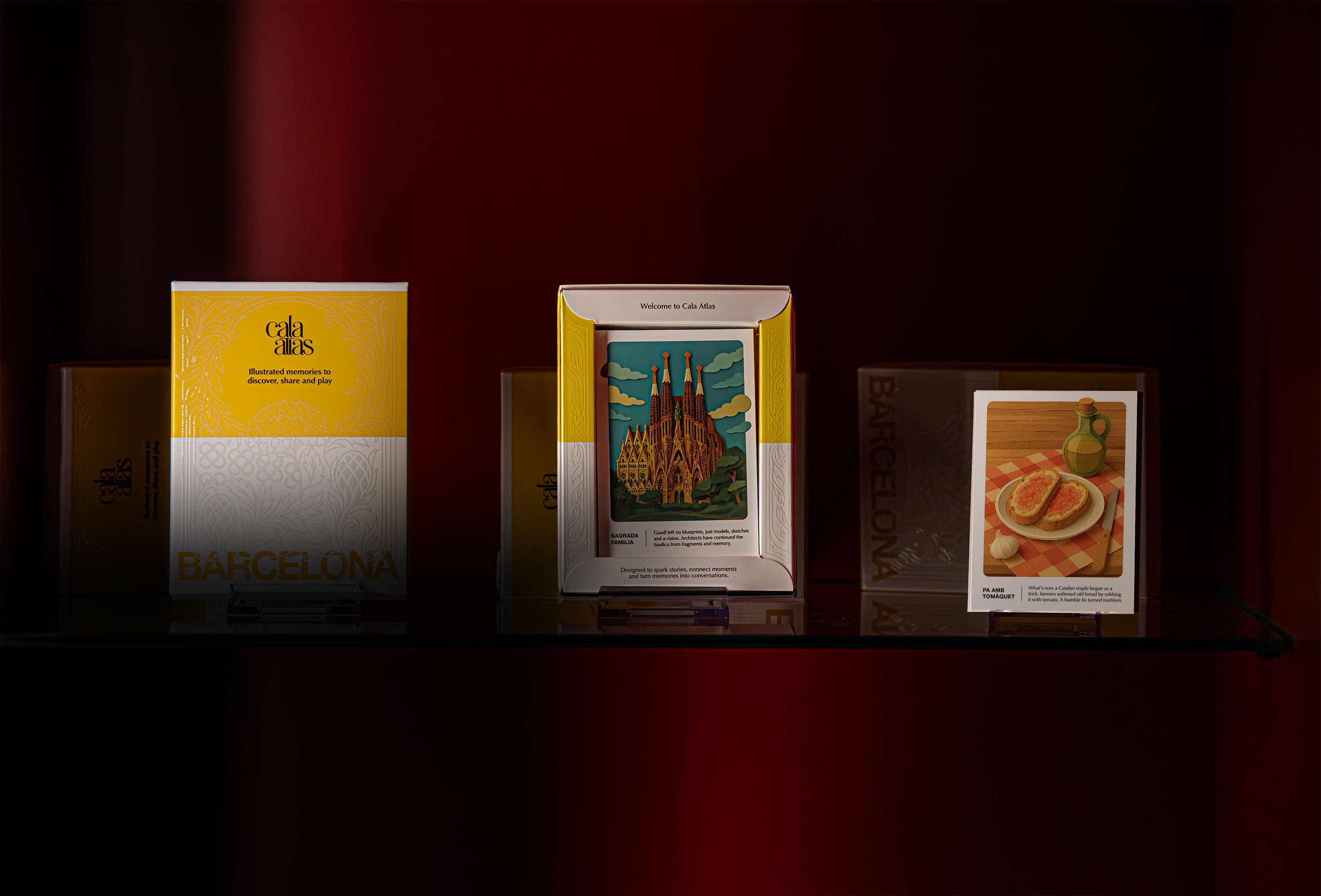 Cala Atlas Barcelona Story Deck boxes and illustrated cards displayed on a shelf, featuring the Sagrada Família and pa amb tomàquet illustrations